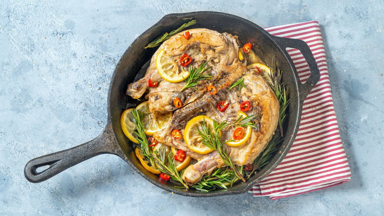 A cast-iron skillet with cooked meat, lemon slices and rosemary.