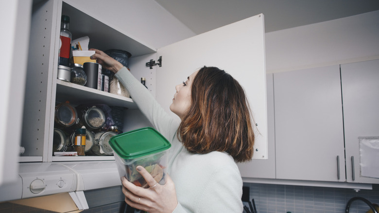 A person puts things away in a kitchen cabinet