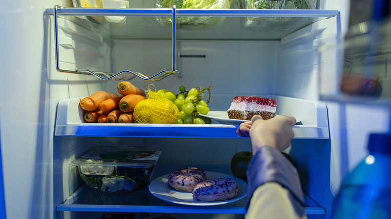 Refrigerator with a variety of produce, greens, cake, and donuts