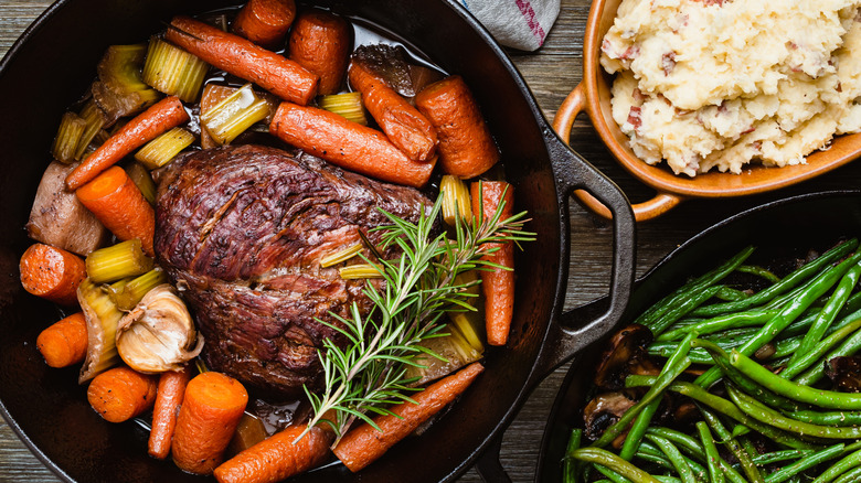 Pot roast in a cast iron skillet with veggies and sides