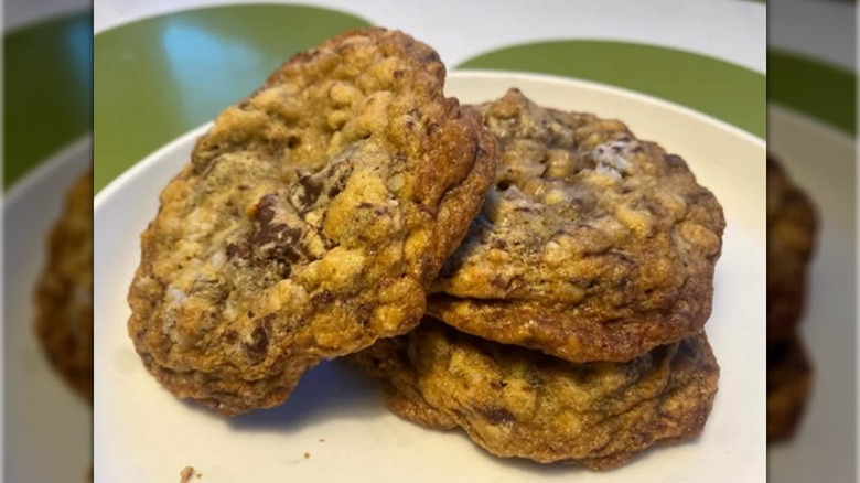 Three salty oatmeal chocolate chunk cookies, two in a stack with the third resting against the stack at an angle, all on a white plate
