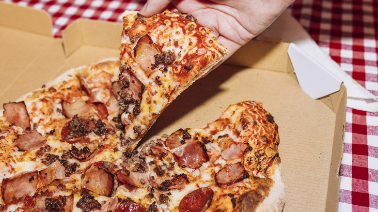A person getting a piece of sausage, ham, and pepperoni pizza from a pizza box