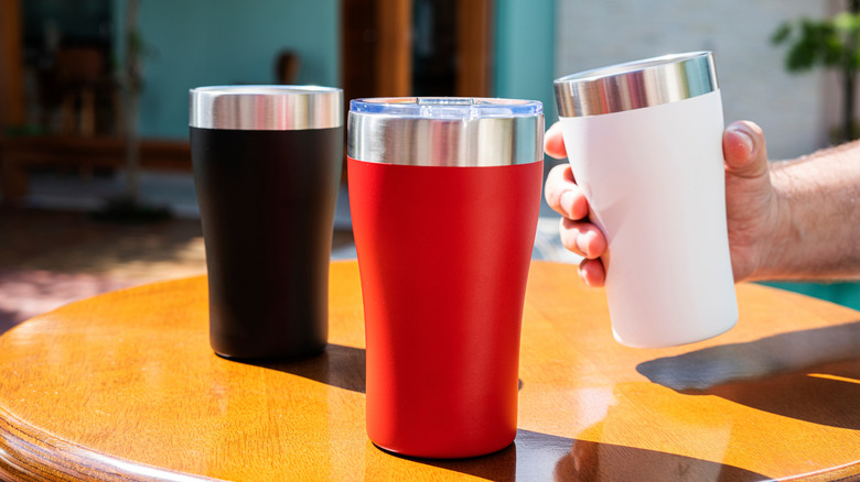 Three thermal mugs in red, black and white on a wooden table
