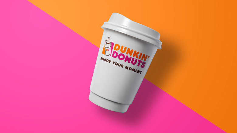 A Dunkin' Donuts coffee cup against a pink and orange background