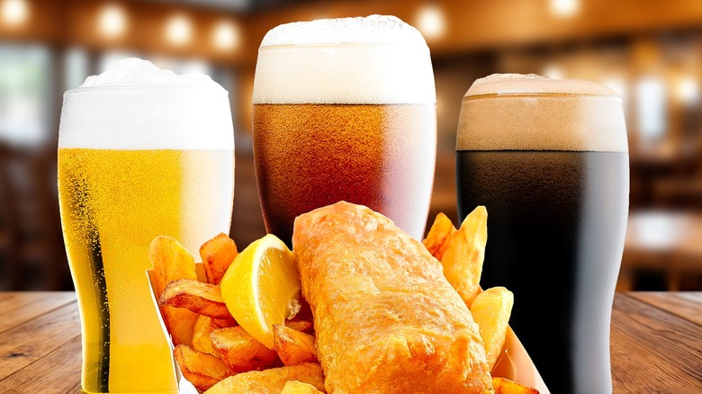 Three glasses of beer and a plate of fish and chips on a bar table