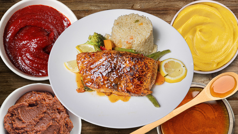 glazed salmon fillets in white plate with four ingredients in bowls and wooden spoon
