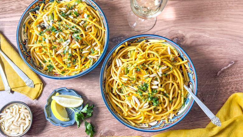 High-protein pasta con le sarde (with sardines) in serving bowls with lemon wedges and slivered almonds