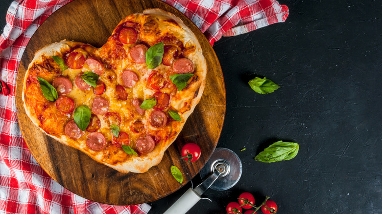 a heart-shaped pizza with pepperoni, tomatoes and basil