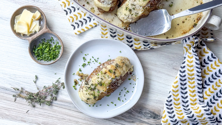 Extra cheesy hasselback potatoes in serving dish on table with cheese,thyme, and chives