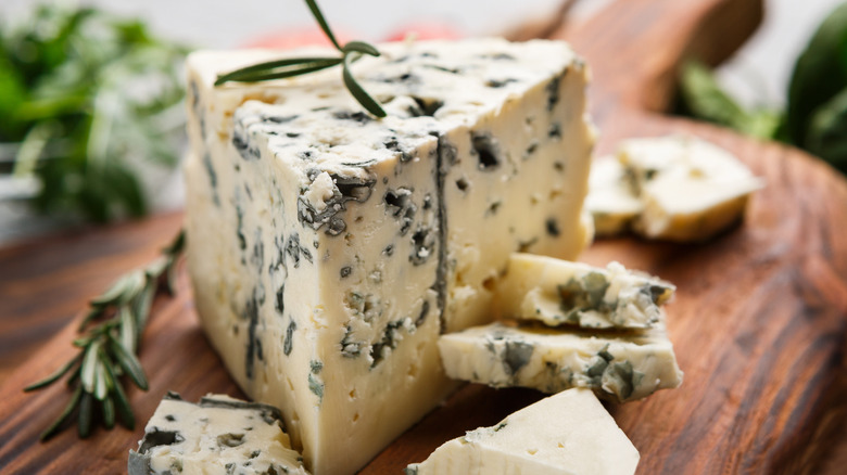 Closeup of a wedge of blue cheese on a wooden board with rosemary sprigs