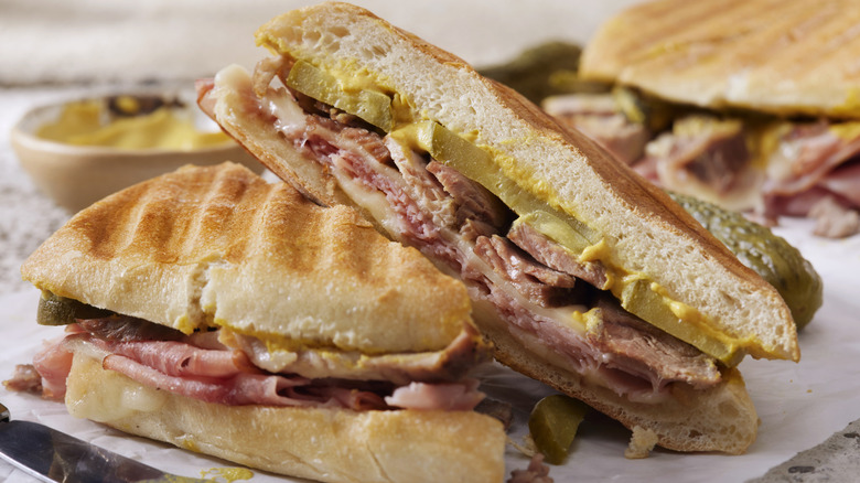 Two slices of Cuban sandwich leaning on each other on a table with another sandwich and mustard