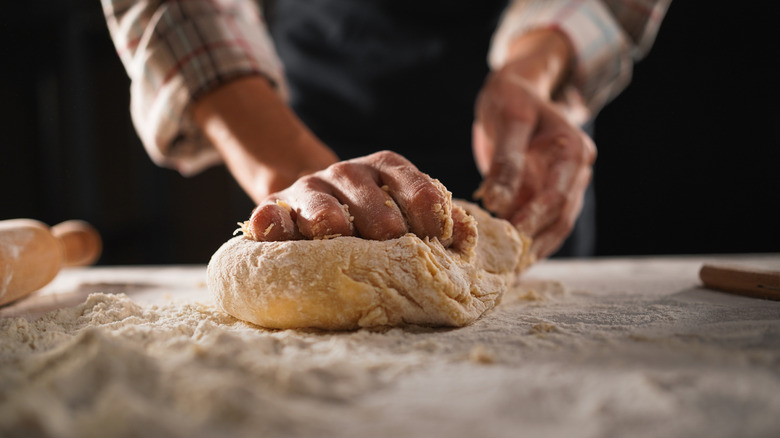 Hands are kneading pasta dough on a floured table.