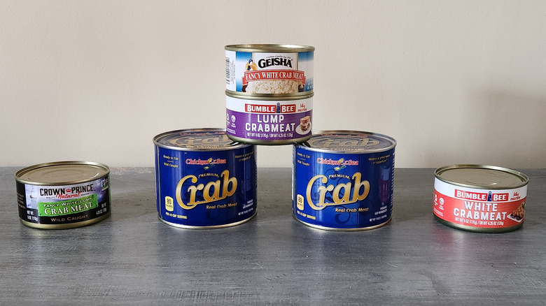 Six cans of crabmeat are arranged on a tabletop.