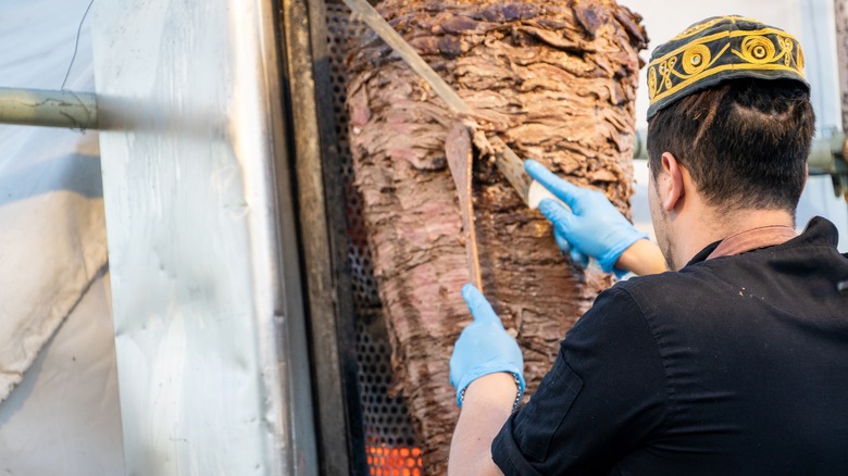 Person preparing shawarma by cutting meat off spit