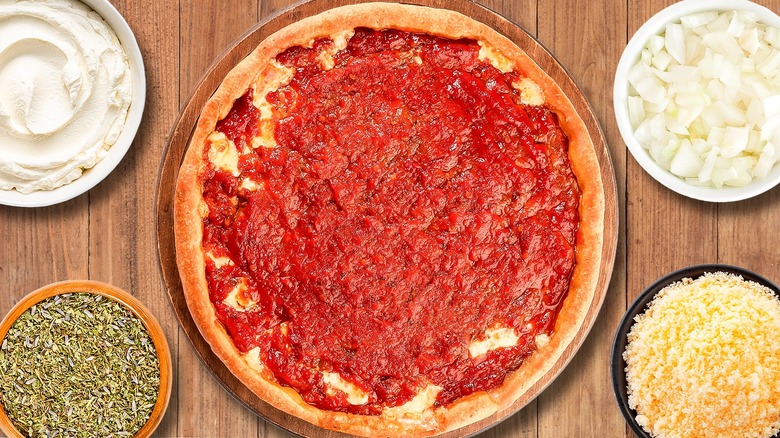 Pizza sauce spread on dough surrounded by ingredients in bowls