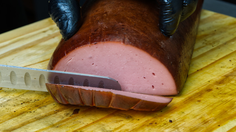 person slicing barbecued bologna with a knife