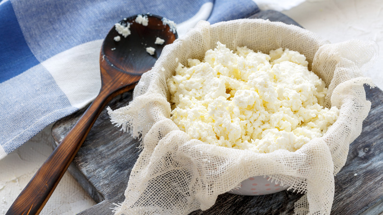 Ricotta cheese in a bowl with cheesecloth and a wooden spoon