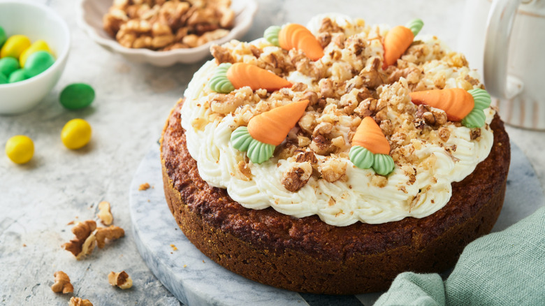 Round carrot cake topped with frosted carrots and walnuts