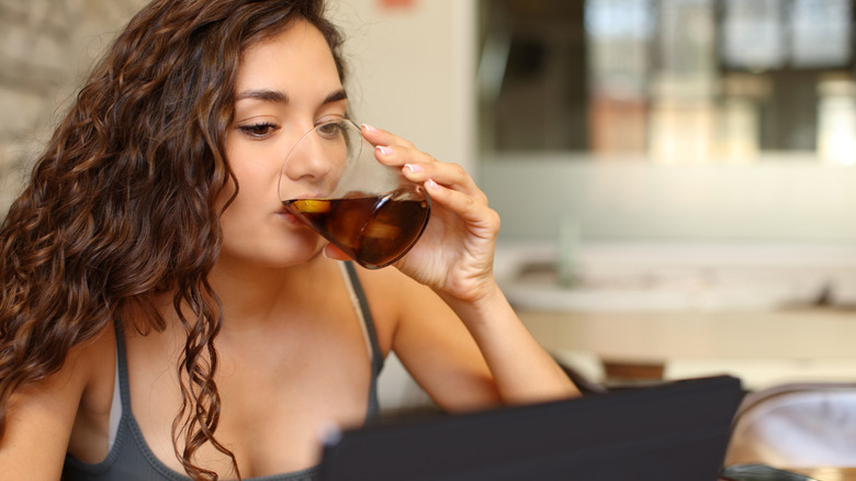 Woman sipping soda working on laptop