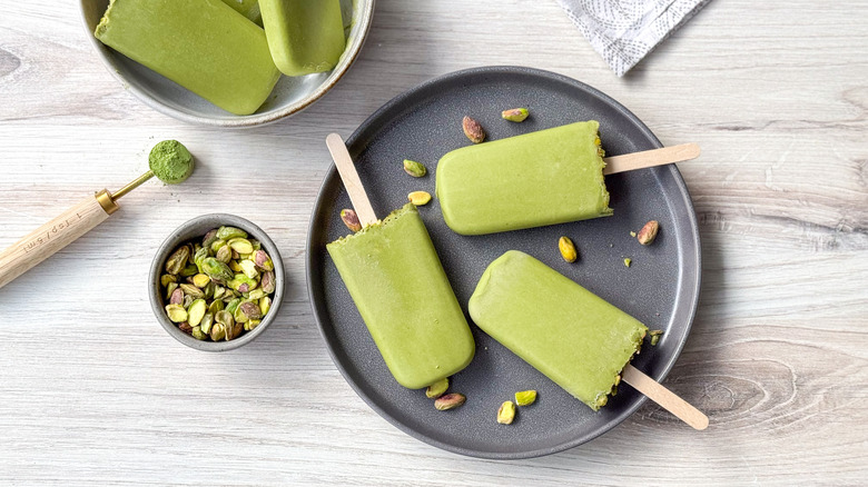 Matcha pistachio popsicles on plate with pistachios and matcha powder