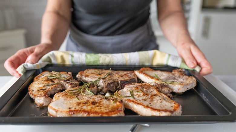 A person holding a pan of baked pork chops