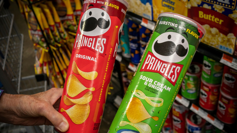 Person holding two cans of different Pringles flavors