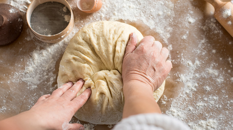 Two hands kneading bread dough on a table with flour