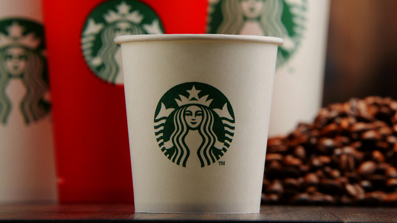Various sized Starbucks cups next to a pile of coffee beans