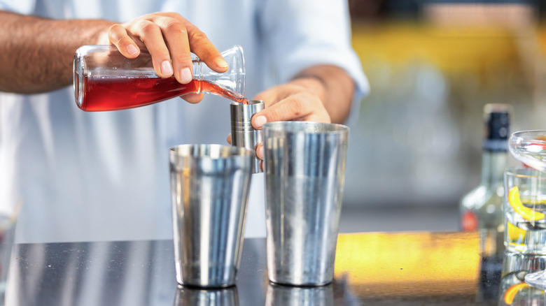 Person pouring red liquid in cocktail shaker