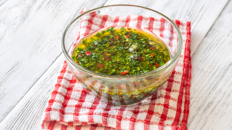 A glass bowl of chimichurri sits on a table.
