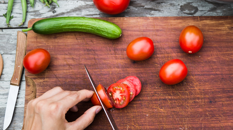 Hand cutting tomatoes on a wooden cutting board