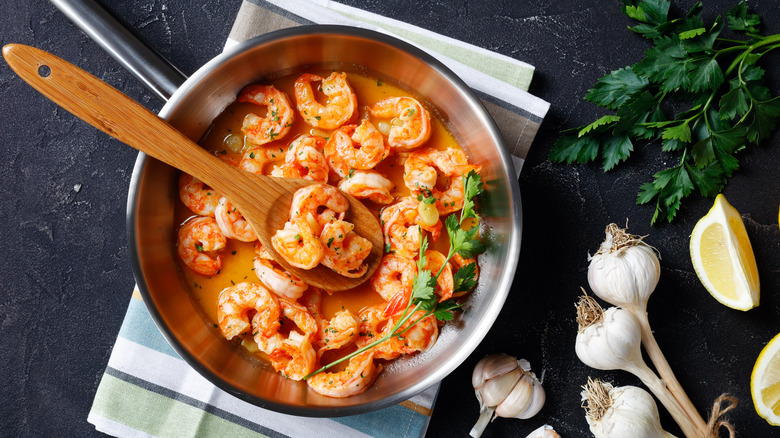 Shrimp scampi in pot with a wooden spoon, garlic, lemon, and herbs