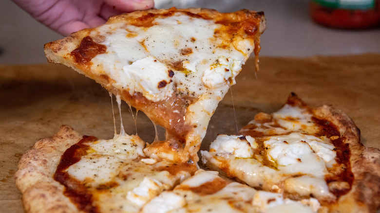 A person pulling a slice of gluten-free pizza away from a whole pizza
