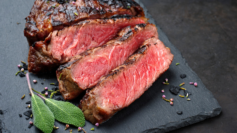 Sliced dry-aged steak on a slate serving board with herbs
