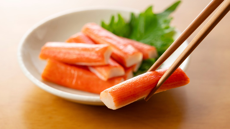 Chopstick holding imitation crab stick in front of a plate