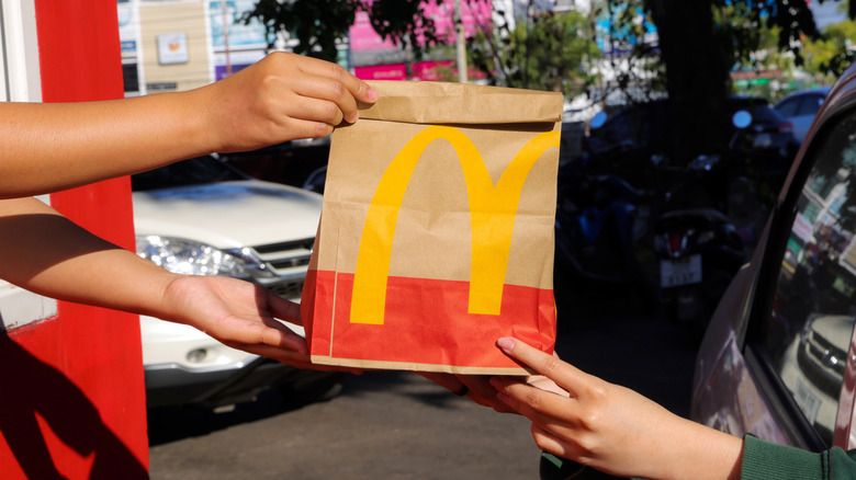 person in car receiving a McDonald's bag from drive-thru window