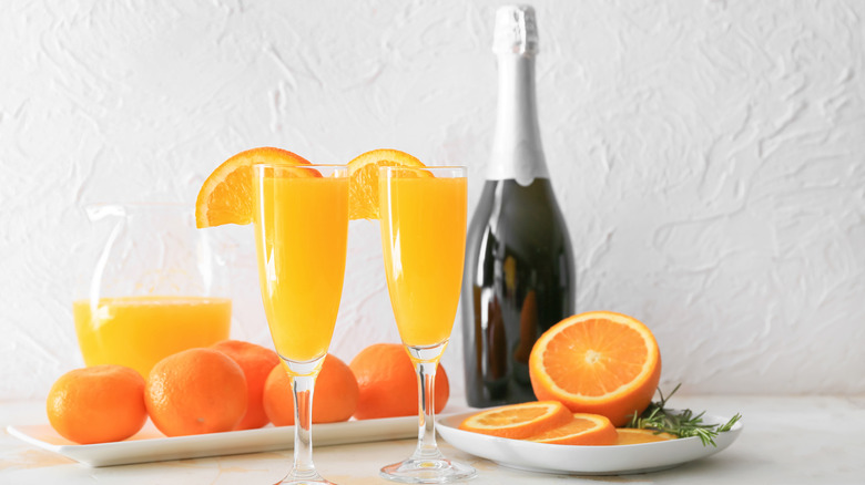 Two mimosas with bottle of bubbly and oranges