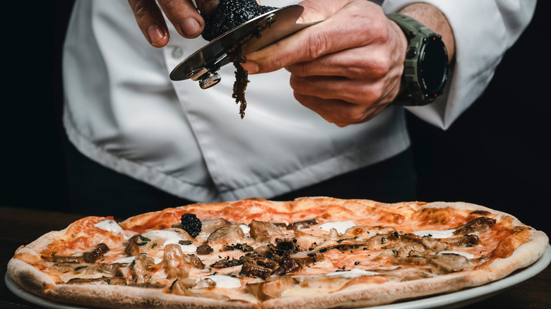 Chef shaving black truffles on pizza