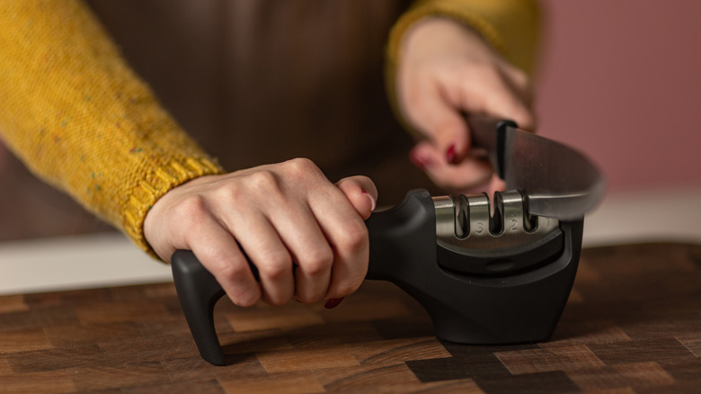 Person in mustard color sweater sharpening knife on wooden table