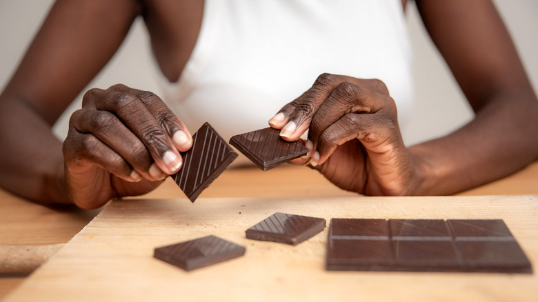 woman breaking dark chocolate bar pieces