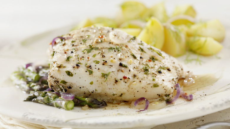 A poached halibut filet plated with asparagus and lemon.