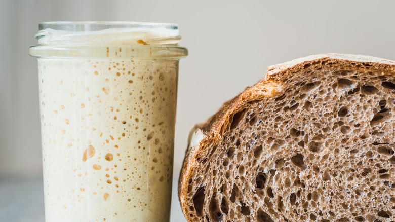 A jar of sourdough starter sits next to a loaf of bread.