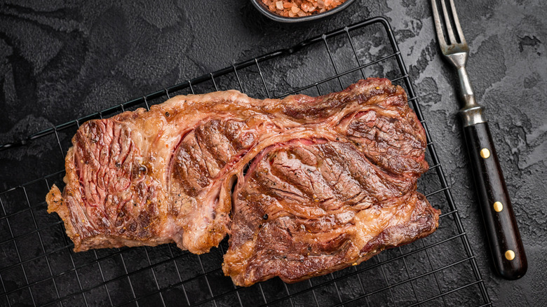Cooked chuck eye steak on a cutting board with a bowl of salt and a fork