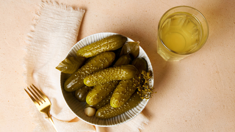 A bowl of pickles next to a glass of pickle juice.
