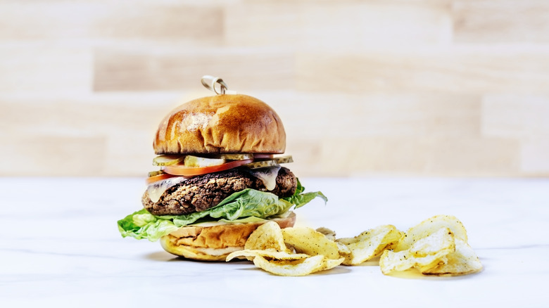 burger with pickles on it next to potato chips
