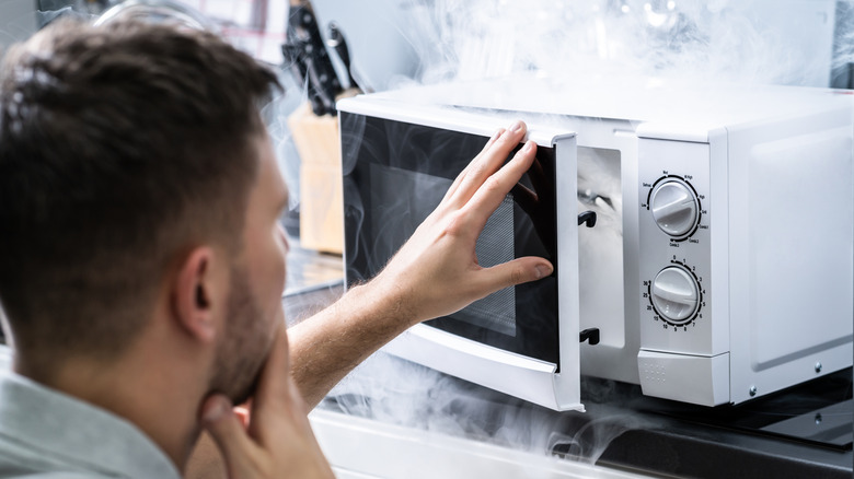 Concerned man opening a microwave with smoke inside