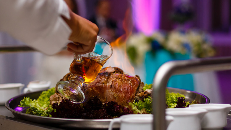 Chef pouring bourbon over a roast