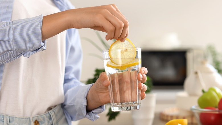 A person putting a lemon slice in water