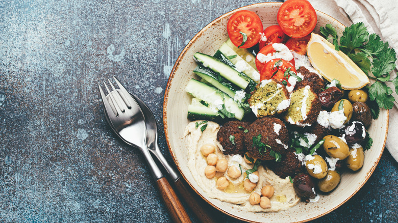 A bowl of falafel served alongside fresh vegetables and hummus.
