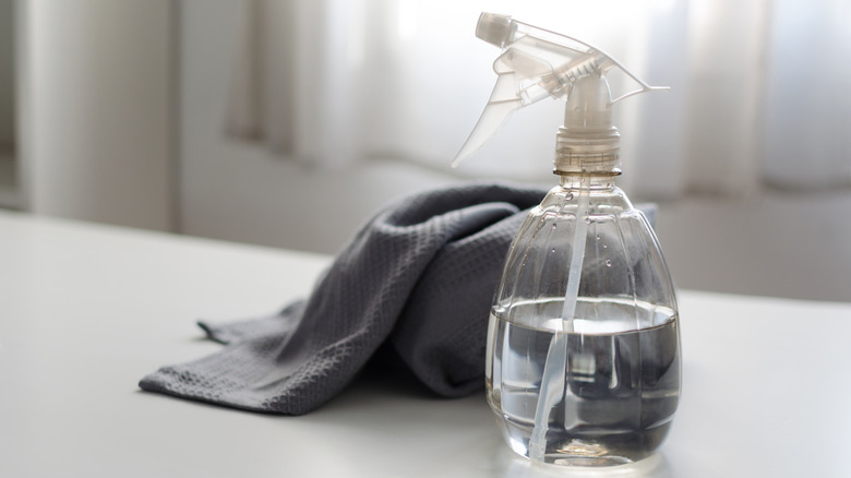 Clear spray bottle filled with vinegar and water next to gray cloth on white table